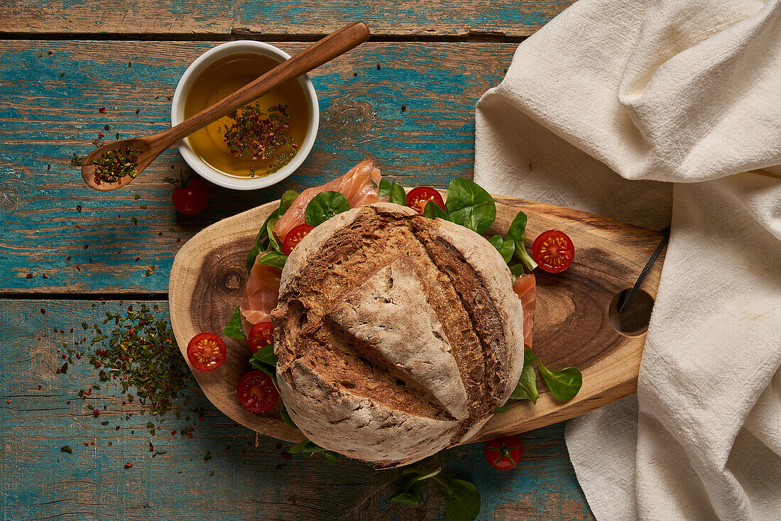 Draufsicht auf selbstgebackenes Sauerteigbrot mit Lachs, serviert auf einem hölzernen Schneidebrett mit Kirschtomaten auf einem schäbigen Tisch