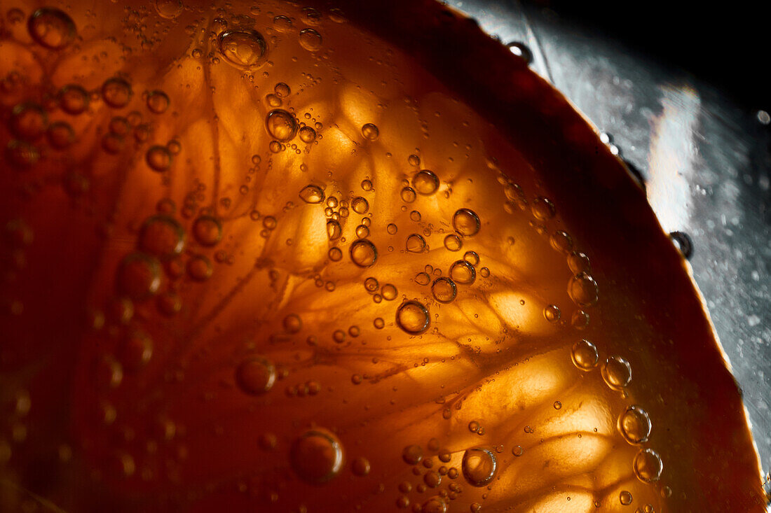 Close-up gin and tonic cocktail with slice of fresh orange bubbling in glass