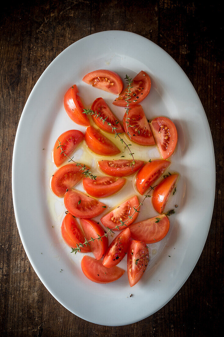 Blick von oben auf appetitliche Tomatenstücke mit grünen Kräutern, die auf einem Teller auf einem Holztisch serviert werden