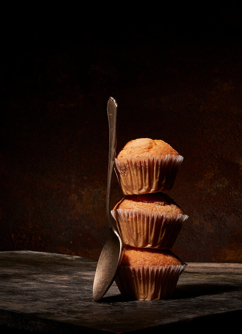 Tasty sweet baked muffins stacked on top of each other near spoon on black background