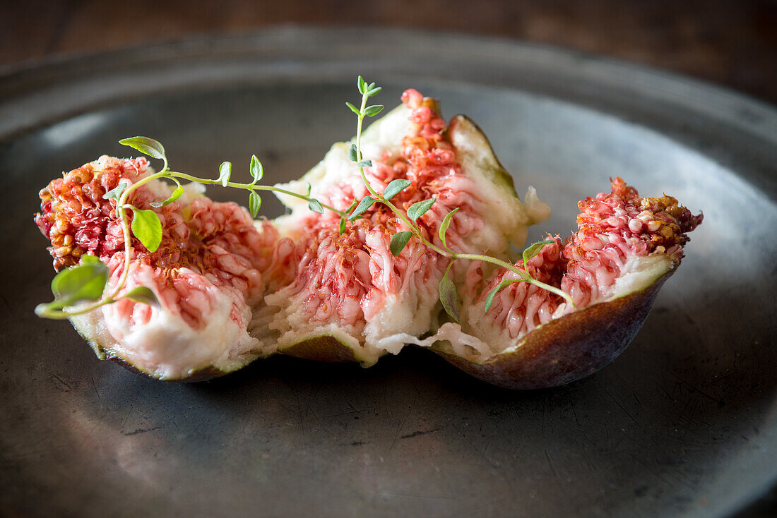 Closeup of tasty ripe fig slices with aromatic thyme sprigs on plate on wooden surface