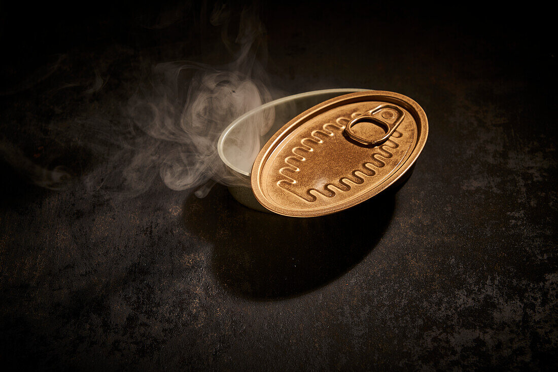 From above of empty tin can with opened lid placed on black background with smoke in room with dim light