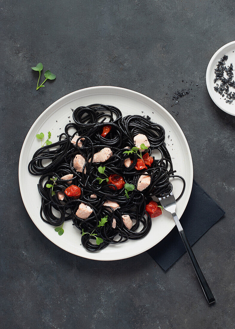 Von oben schwarzer Tinte Spaghetti mit Lachs in Keramikteller auf dunklem Hintergrund
