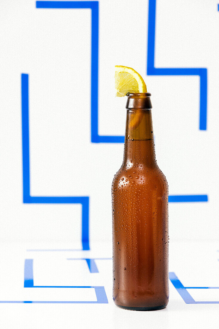 Blick von oben auf eine Glasflasche mit kaltem Bier und einer Scheibe frischer Zitrone im Flaschenhals auf weißem Hintergrund