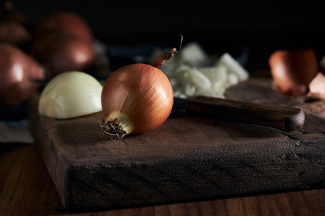 Rustikale Schale mit geschnittenen Zwiebelstückchen neben Messer auf Holztisch in Küche