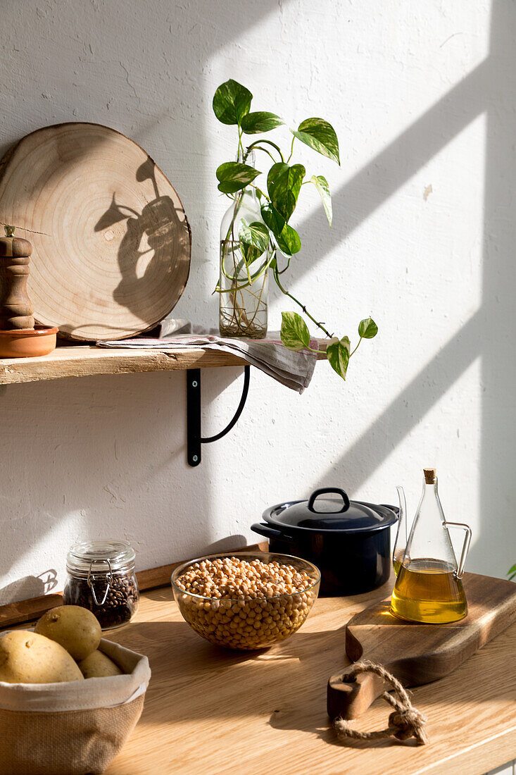 Verschiedene Zutaten und Utensilien auf einem Holztisch während des Kochvorgangs in einer Küche mit weißen Wänden und minimalistischem Interieur im natürlichen, umweltfreundlichen Stil