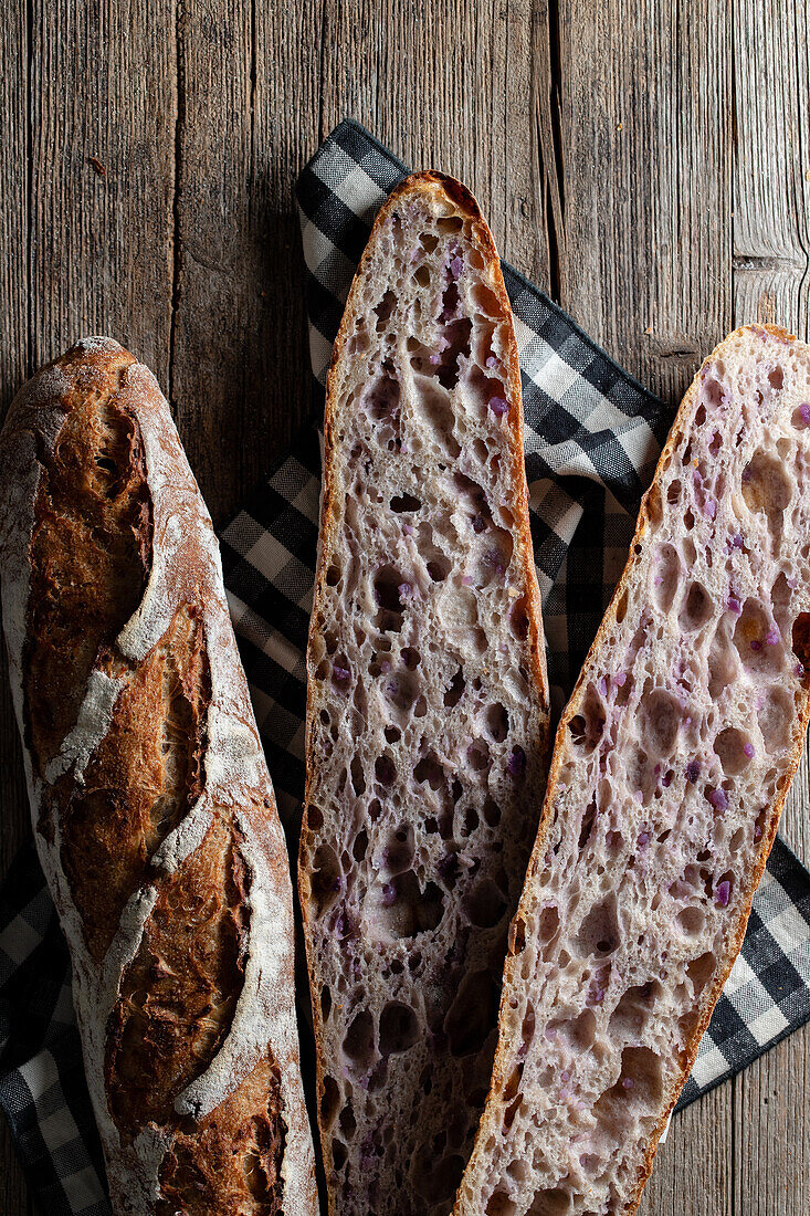 Top view of cut and whole sourdough baguettes with crunchy crust placed on wooden table