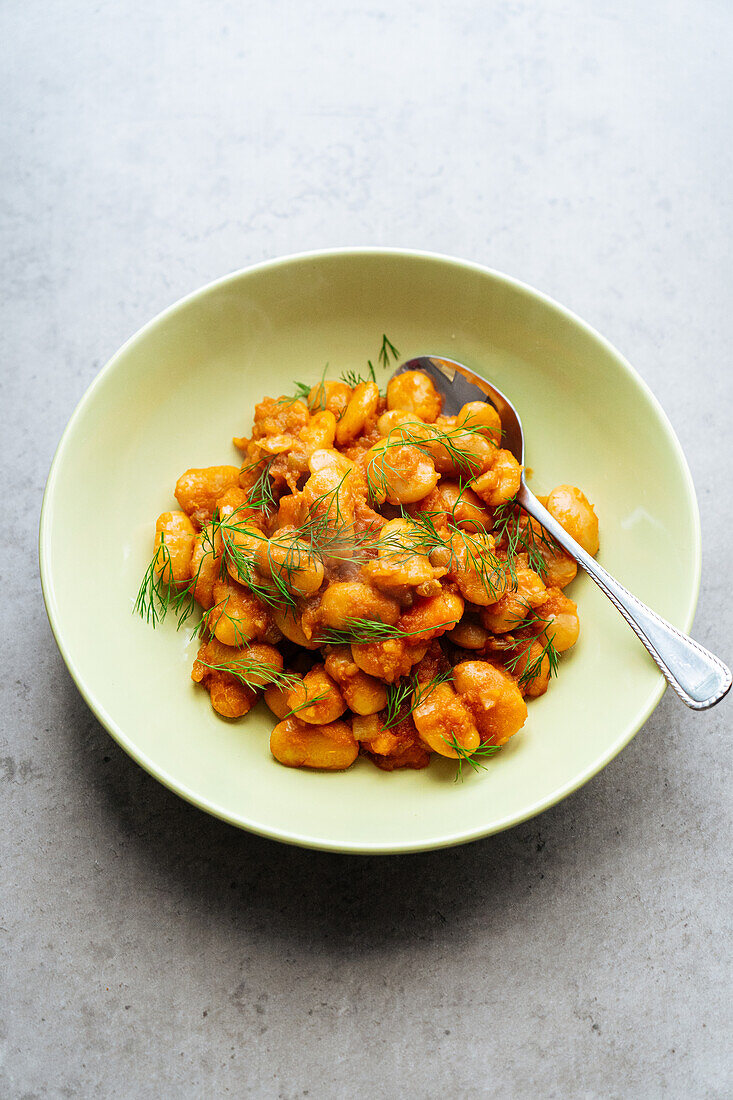 From above of delicious traditional Greek giant naked beans in tomato sauce served in plate on gray background in kitchen