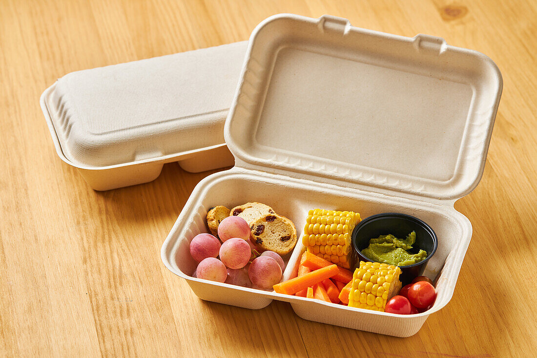 From above of lunch boxes with healthy food including crackers carrot sticks grapes cherry tomatoes with broccoli walnut and tangerine on yellow background