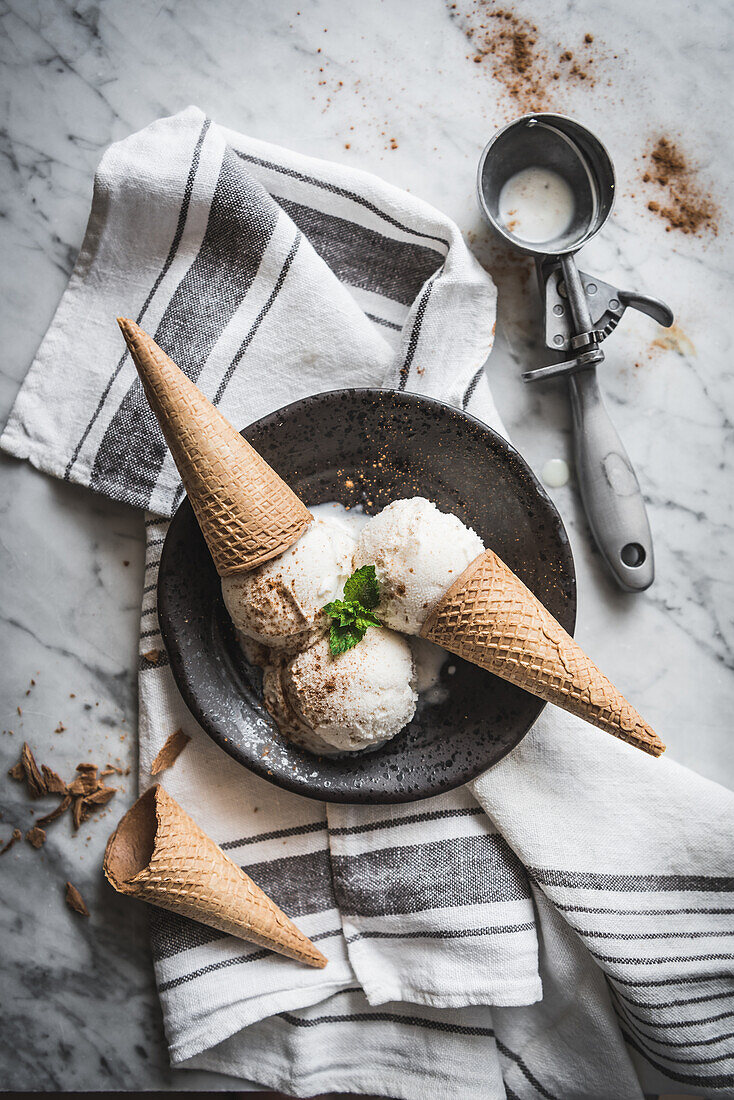 From above of waffle cones with meringue milk gelato scoops and fresh mint leaves with cinnamon powder on top