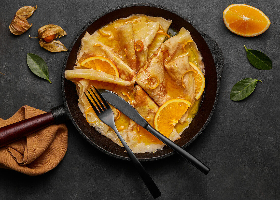 Von oben hausgemachte Crêpes Suzette mit Orangenlikör und Orangenscheiben auf einem Teller mit Messer und Gabel auf einer Betonfläche serviert