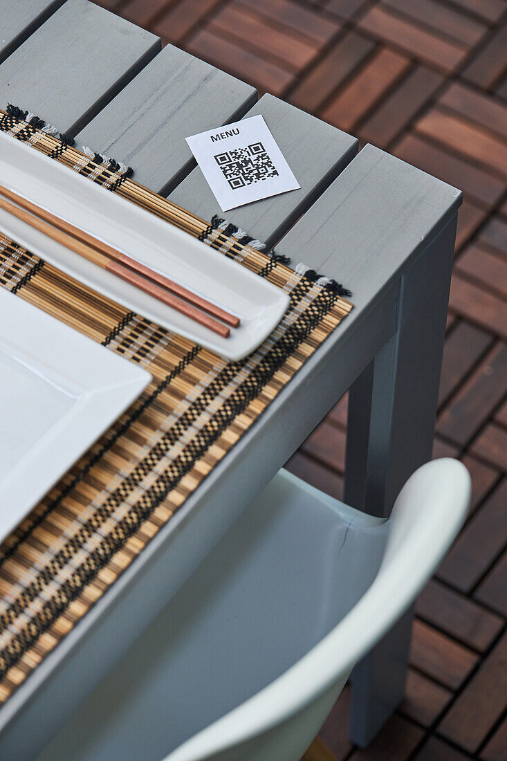 Blick von oben auf ein Stück Papier mit QR-Code der Speisekarte, die auf einem Tisch mit Stäbchen und Teller in einem asiatischen Restaurant liegt