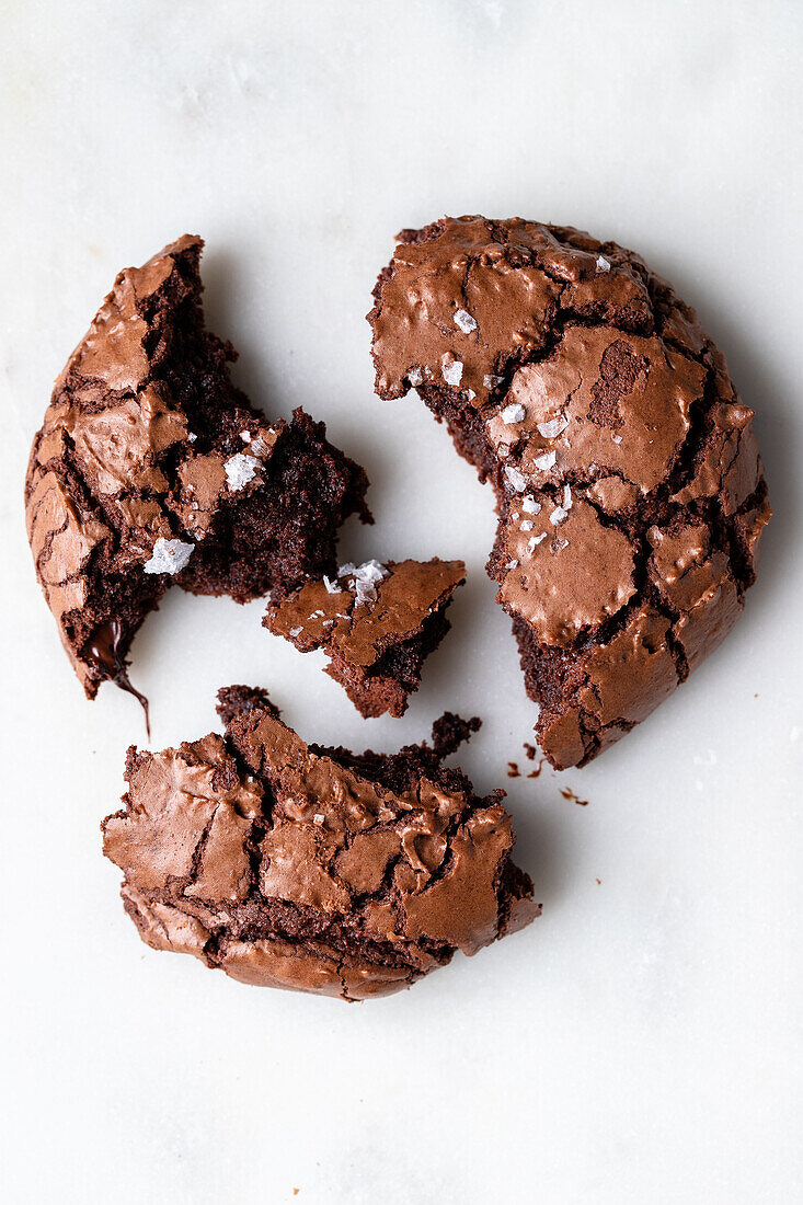 Draufsicht auf einen hausgemachten gebrochenen süßen Schokoladen-Brownie-Keks mit Rissen und Krümeln auf weißem Hintergrund in einer hellen Küche