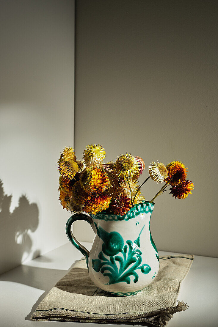 Strauß frischer Erdbeerblumen in Keramikkrug auf einem Tisch in einem Raum mit Sonnenlicht
