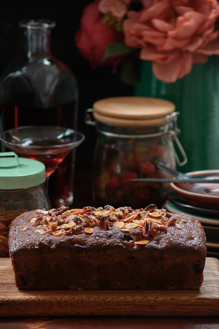Tasty baked pound cake topped with almond flakes served on wooden cutting board on table with alcohol drink and berries