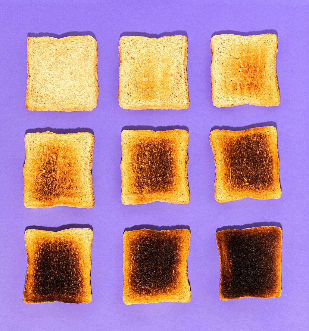 Top view of slices of bread ranging from fresh and soft to burnt against violet background