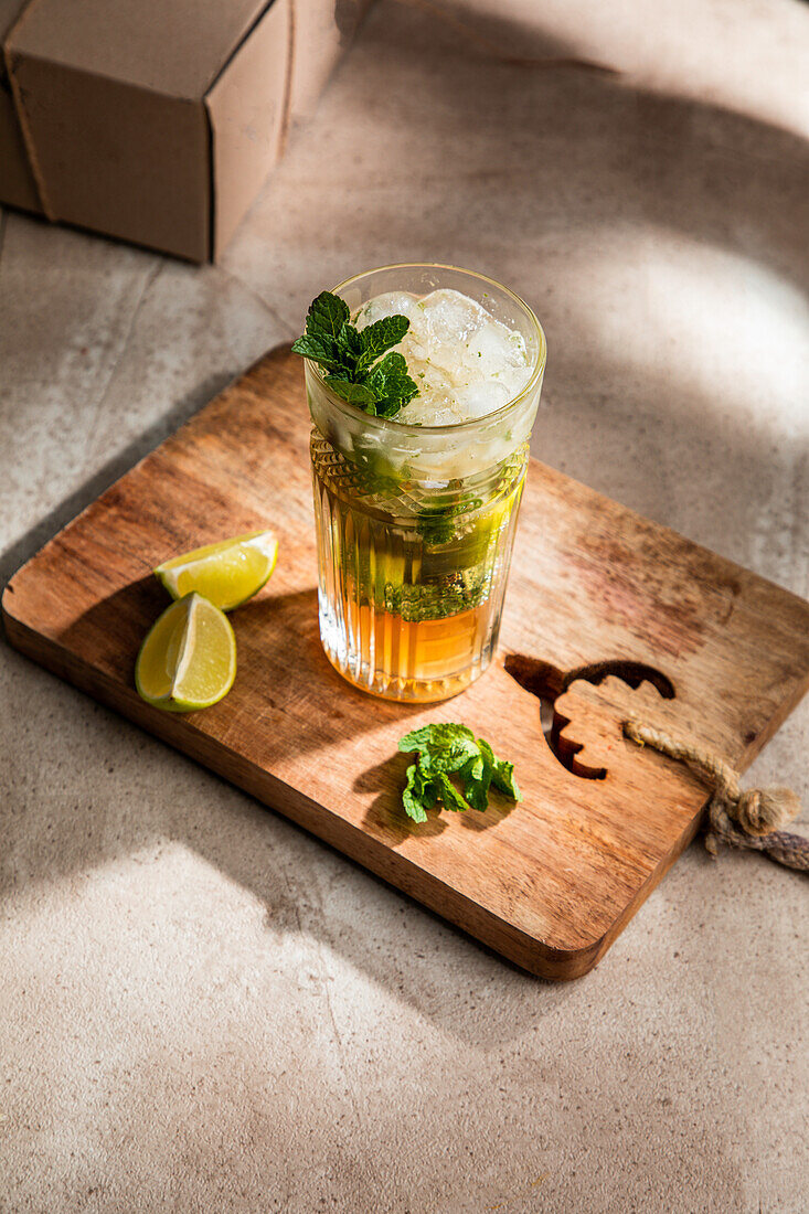 From above of refreshing cold alcoholic mojito with ice mint leaves and cut lime on wooden board