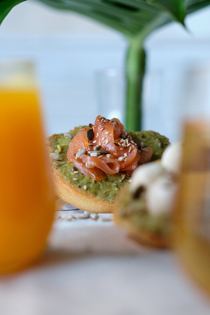 Glasses of juice and herbal tea served on wooden table with assorted healthy avocado toasts with cheese and salmon during breakfast in outdoor cafe
