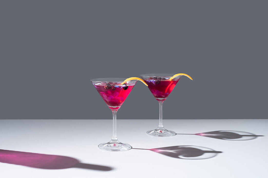 Composition of glass filled with red fruit cocktail with orange zest placed on concrete table against grey background