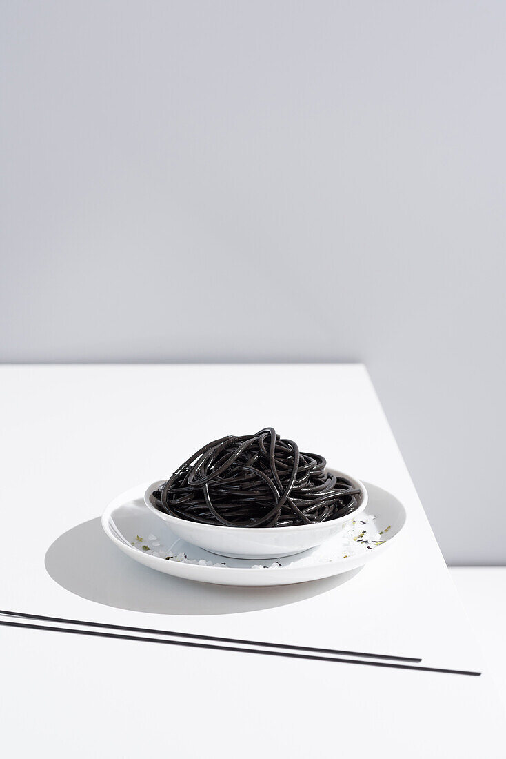 From above of ceramic bowl with delicious spaghetti with black squid ink with chopsticks on grey background