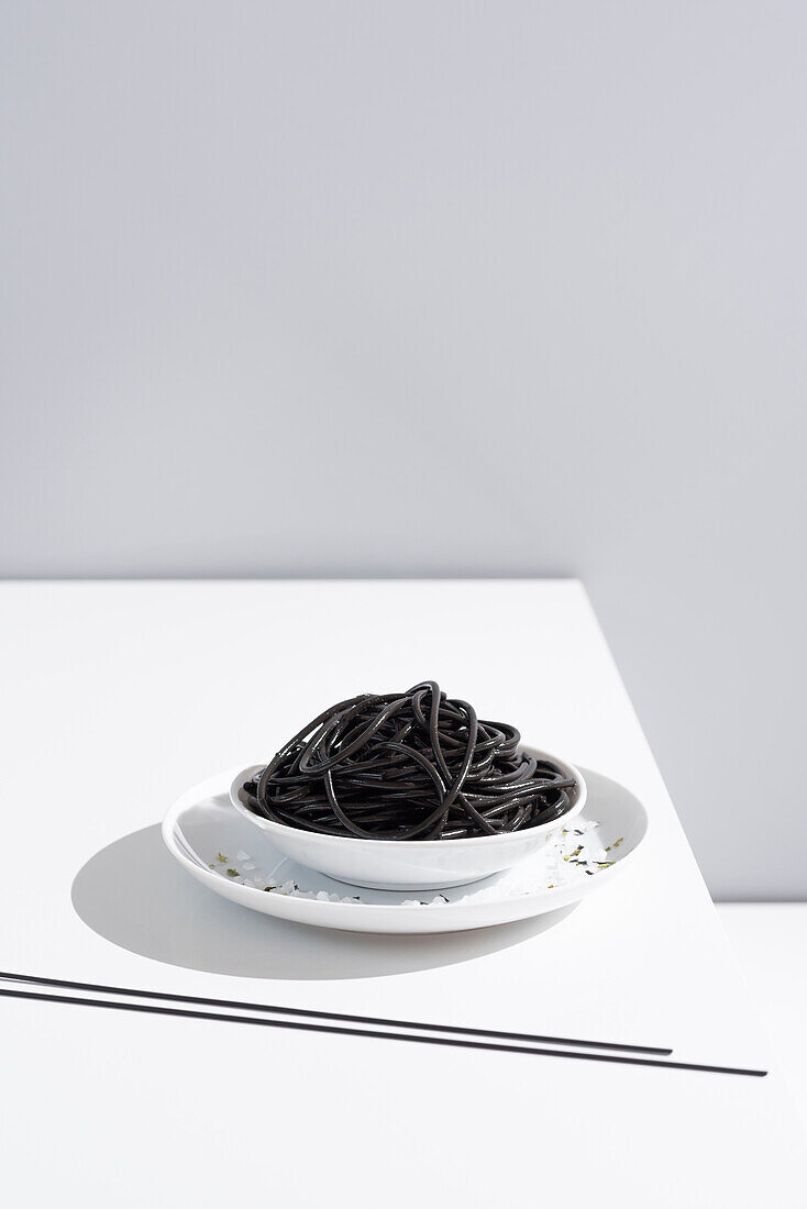 Von oben auf Keramikschale mit leckeren Spaghetti mit schwarzer Tintenfischtinte mit Stäbchen auf grauem Hintergrund