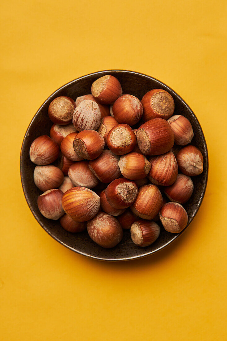 Top view of fresh unpeeled hazelnuts placed in bowl on yellow background