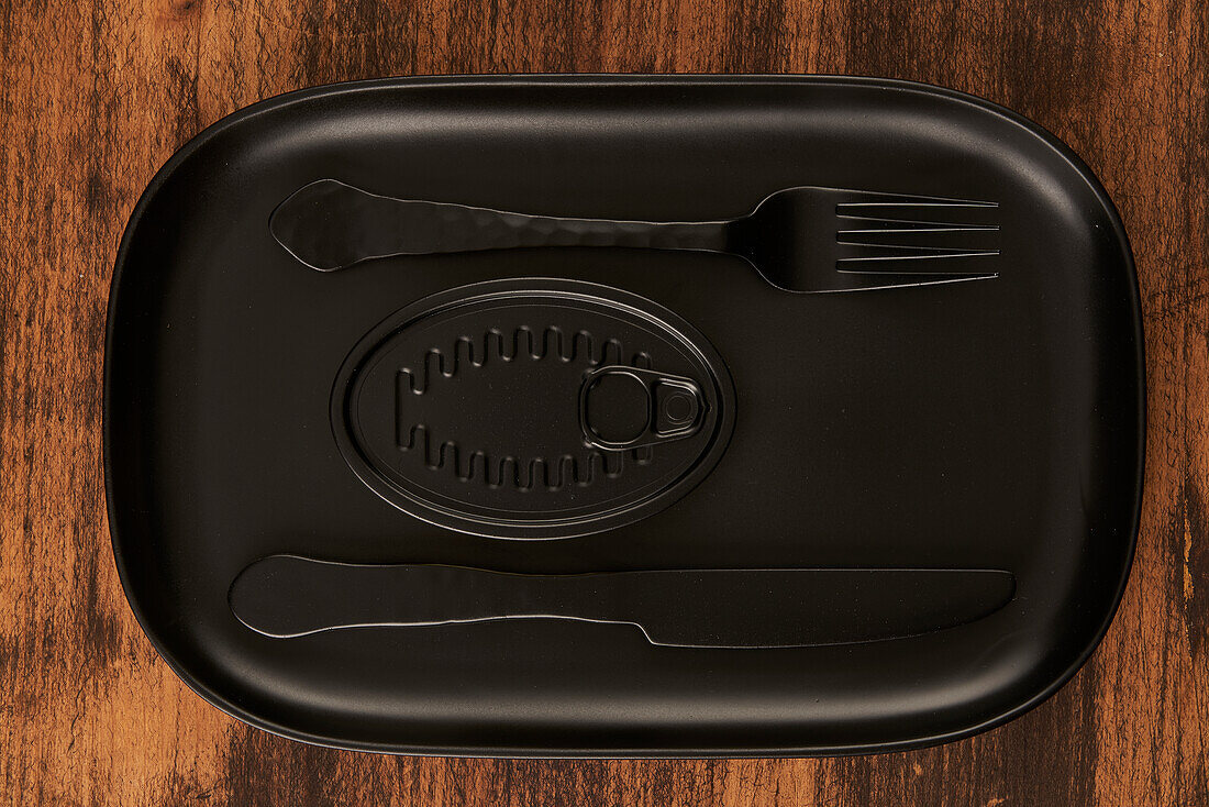 Draufsicht auf eine schwarze Gabel und ein Messer, die neben versiegelten Konserven auf einem rechteckigen schwarzen Tablett liegen