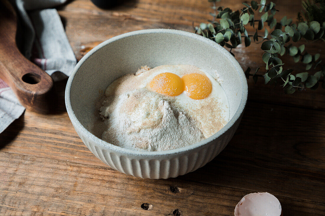 From above bowl with eggs and cream mixed with bread crumbs and flour on wooden table during pastry preparation