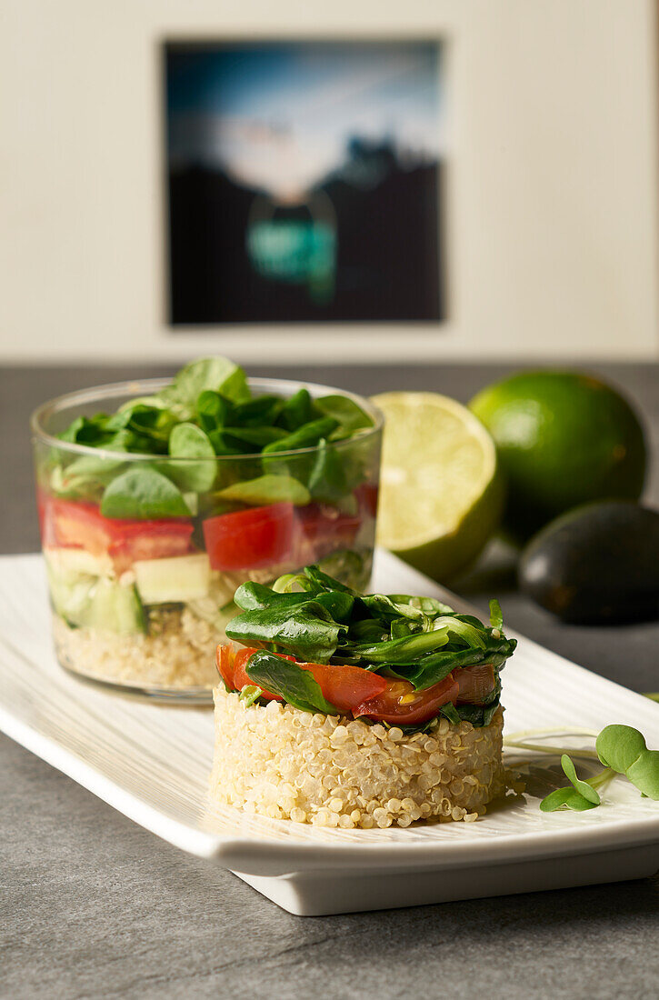 Blick von oben auf einen leckeren Salat aus Reis und Gemüse in runder Form und im Glas serviert auf einem weißen Teller neben grünen Limetten auf einem grauen Tisch