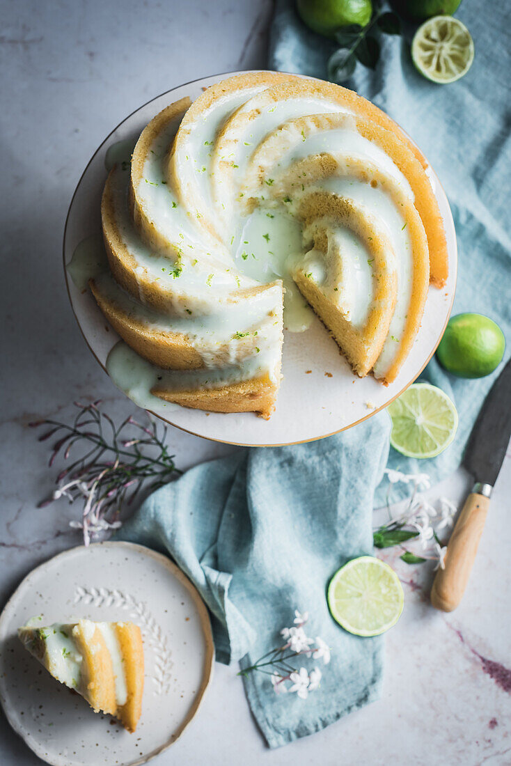 Top view of tasty lime sponge cake served on white plate near flowers and lime slices