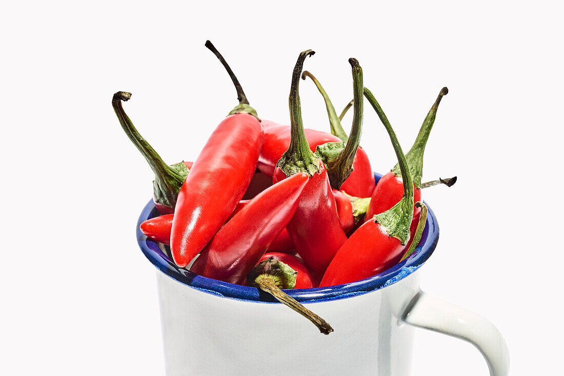 Big ceramic mug full of ripe fresh exotic pepper placed on white background