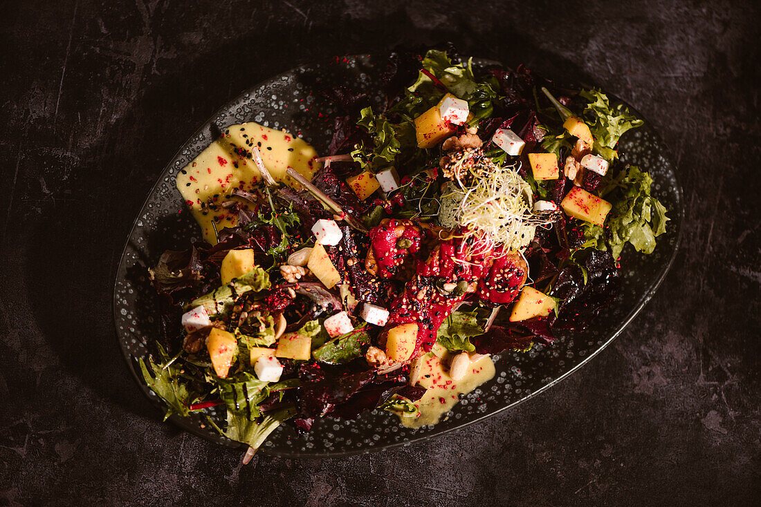 Teller mit leckerem vegetarischem indonesischem Salat mit frischer Mango und Cashew-Käse-Scheiben neben Sojabohnen und Gewürzen, bedeckt mit Basilikum-Vinaigrette