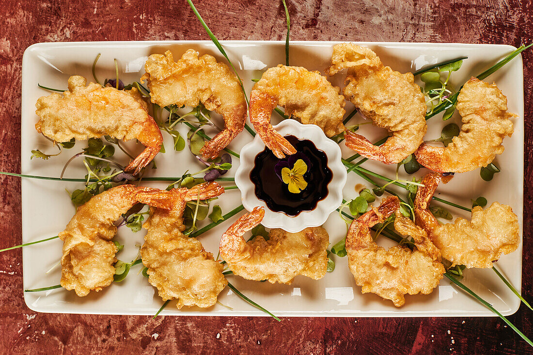 From above tasty shrimp tempura with greens and soy sauce served on plate on restaurant table