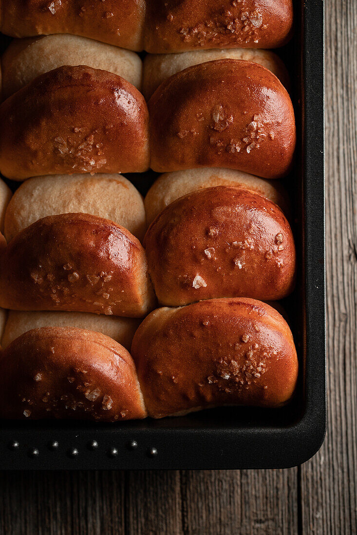 Top view of baked tasty soft dinner rolls on tray placed on wooden surface in dim light
