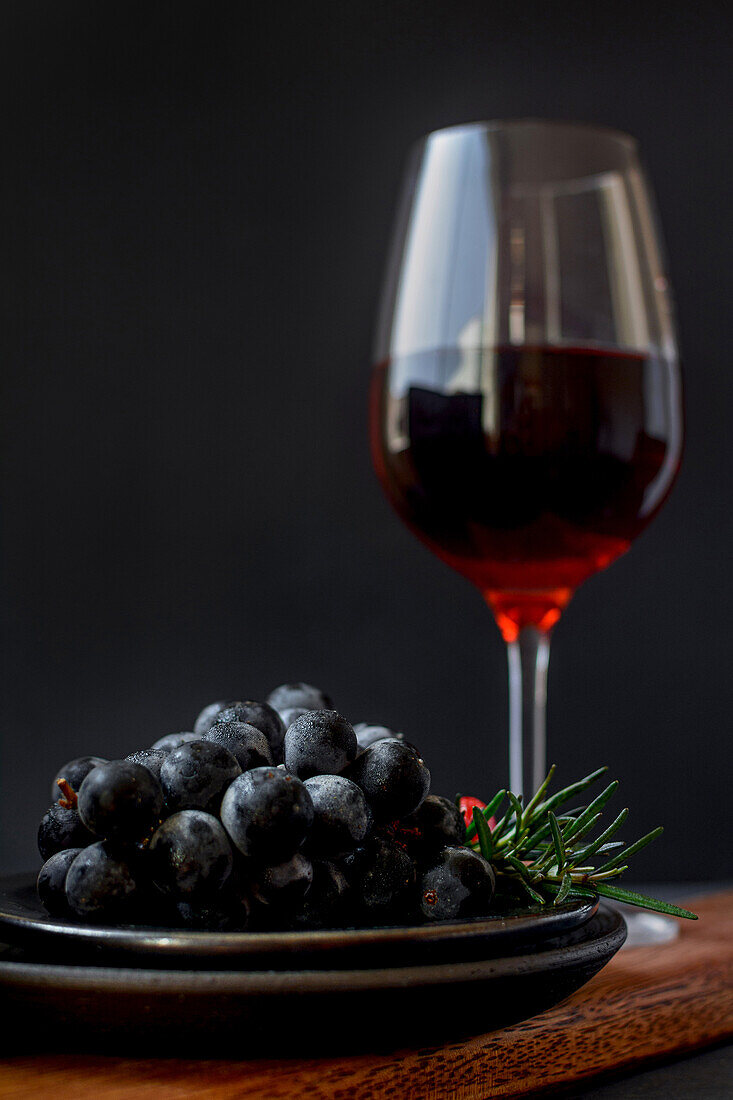 Wine glass placed on table with fresh ripe grapes in studio on black background