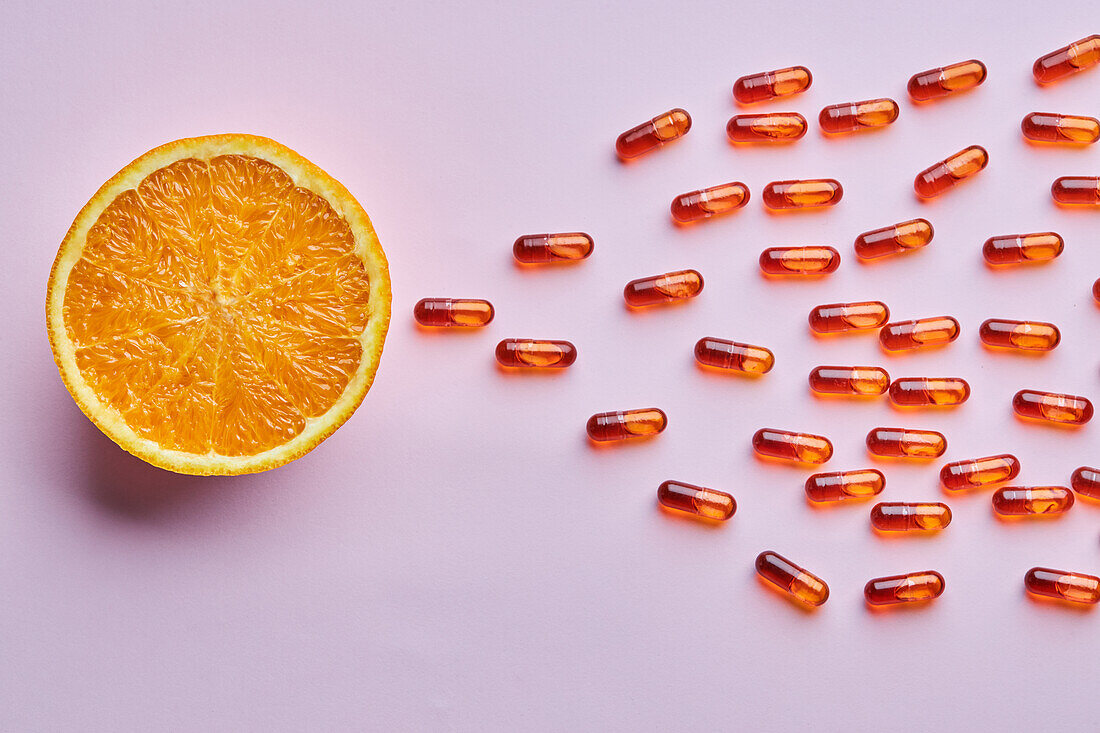 Top view composition of ripe cut oranges arranged on pink surface near scattered pills in light studio