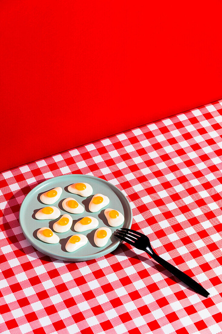 Blick von oben auf einen Teller mit Gelee-Eiern und einer Gabel auf einer rot-karierten Serviette vor einem scharlachroten Hintergrund