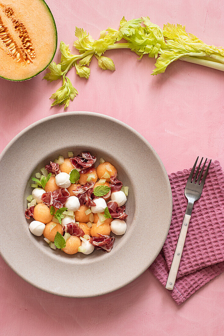 From above exotic melon, mozzarella and prosciutto salad on pink colorful background