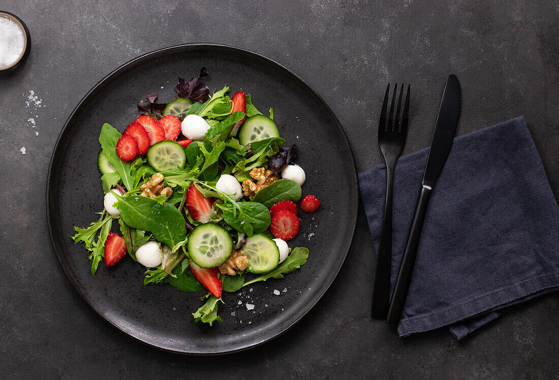 Dish with a summer salad of strawberries and cucumber on a dark table