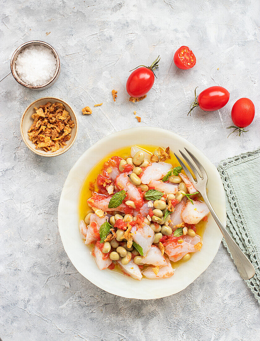 Tomaten- und Kabeljausalat mit reichlich Olivenöl in einem tiefen Teller mit einer Gabel und einer Schale mit gebratenen Zwiebeln