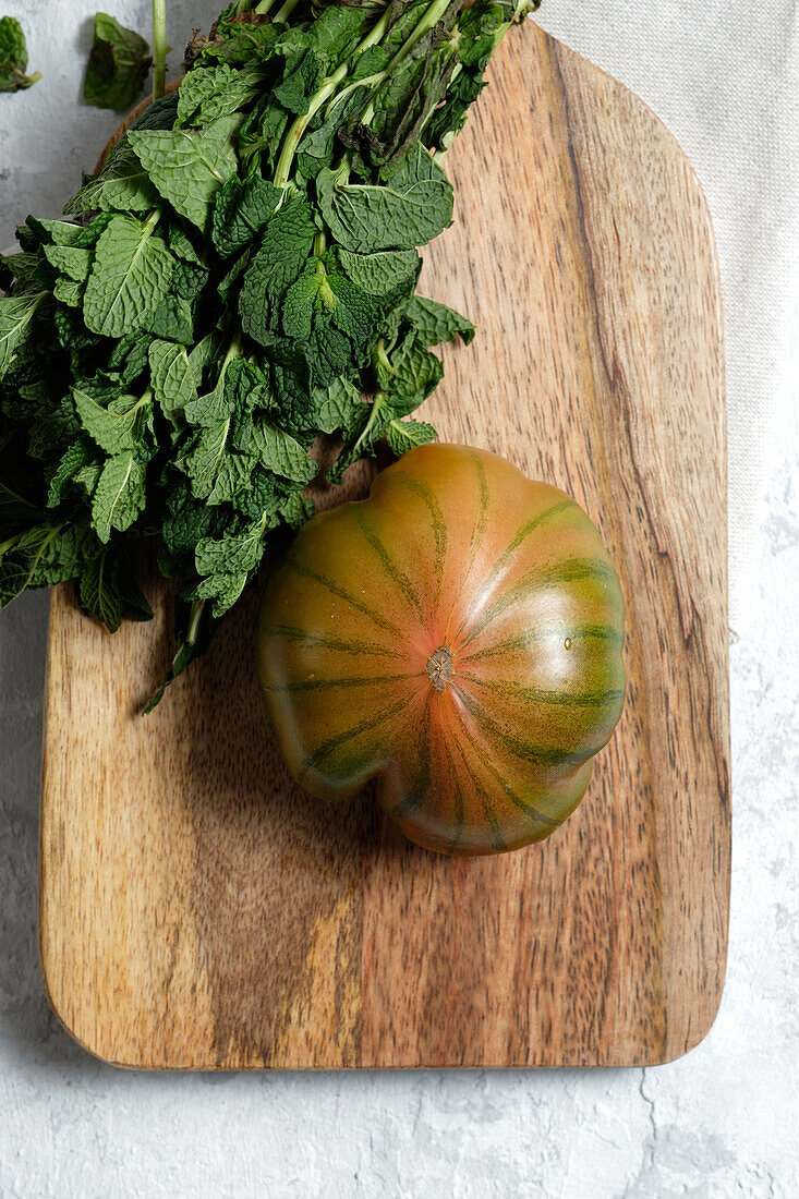 Frische gestreifte grüne und rote Tomaten auf einem Holzbrett mit Minzstängeln