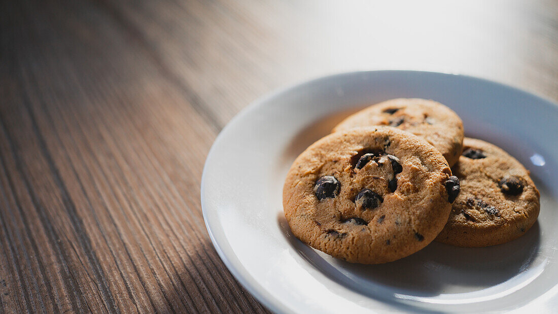 From above of plate with tasty oatmeal biscuits with chocolate chips on wooden table