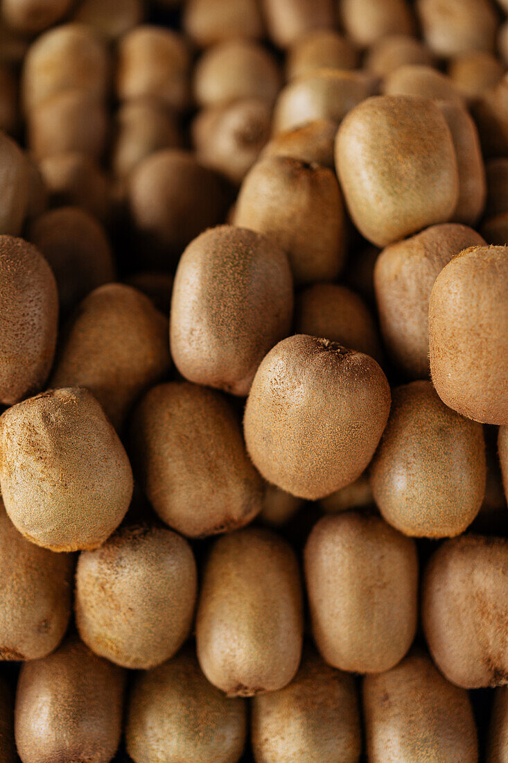 Full frame stack of ripe kiwi with hairy skin stacked on stall in local market during harvesting season on summer day