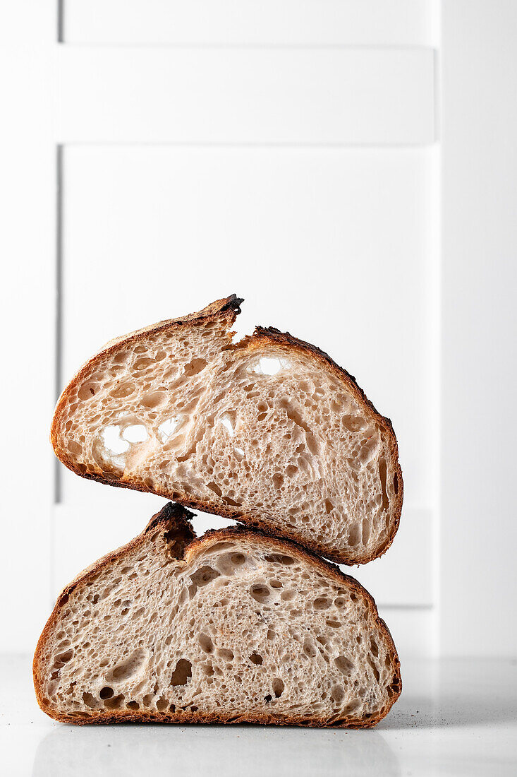 Halves of tasty sourdough bread with brown crust placed on table against white backdrop