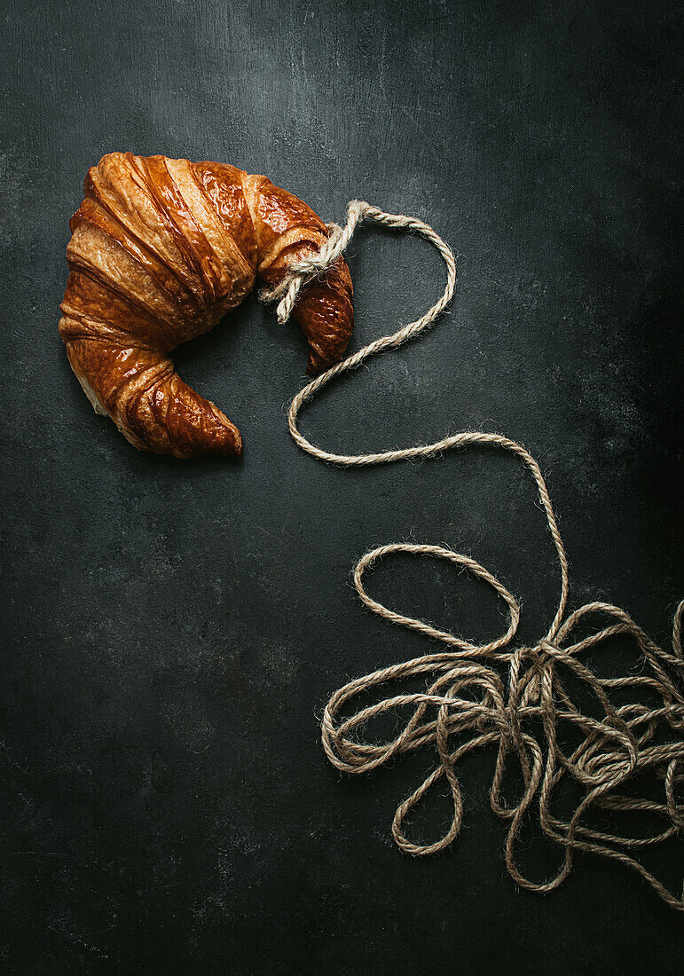 From above of delicious freshly baked traditional croissant wrapped with rope on black background