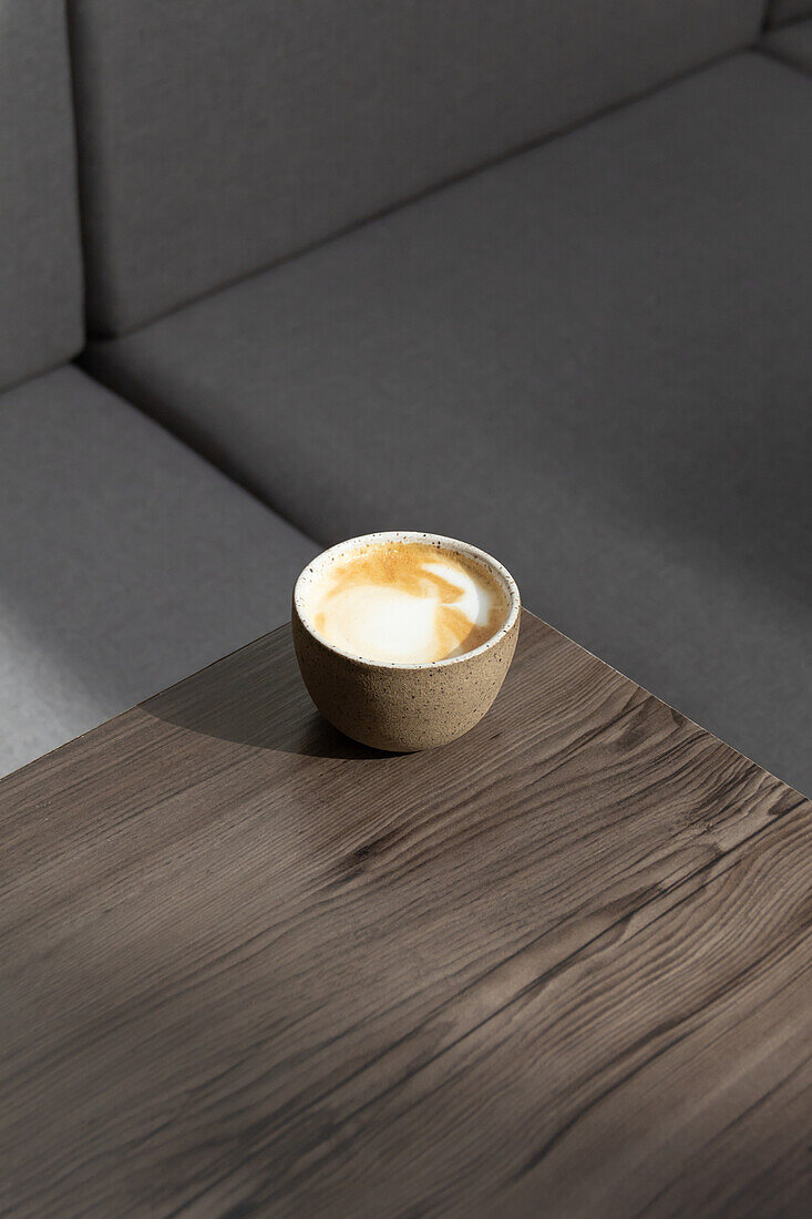 Blick von oben auf frischen aromatischen Cappuccino in einer Keramiktasse, die in einer Ecke eines Holztisches in einem modernen Café steht