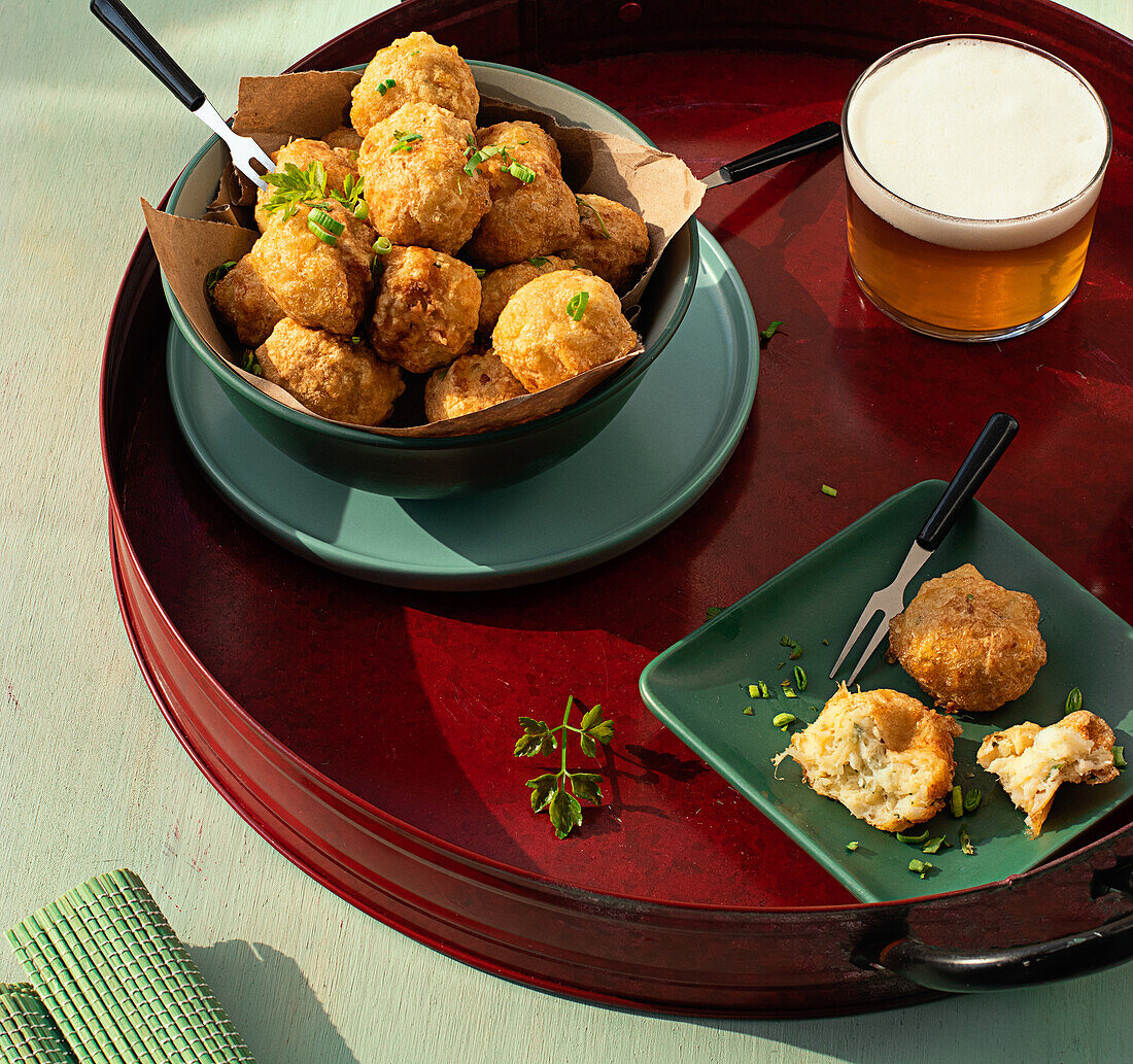 From above traditional codfish fritters server on tray with fresh herbs and glass of beer on green background