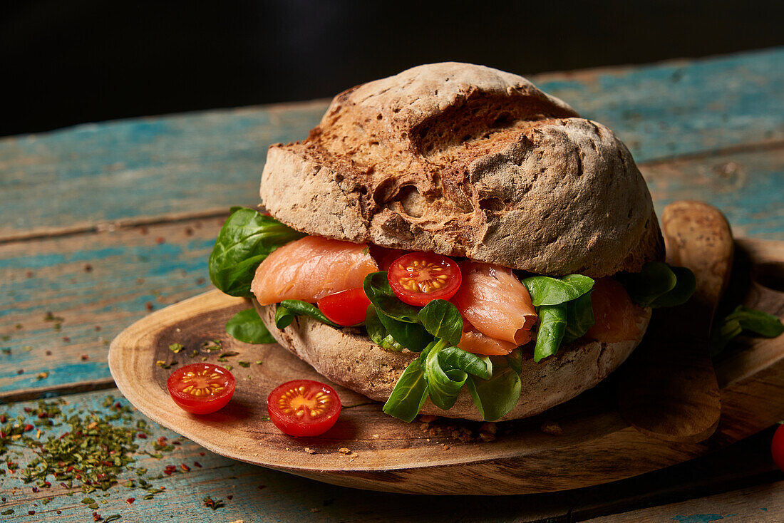 Homemade sourdough bread with salmon served on wooden cutting board with cherry tomatoes and knife on shabby table