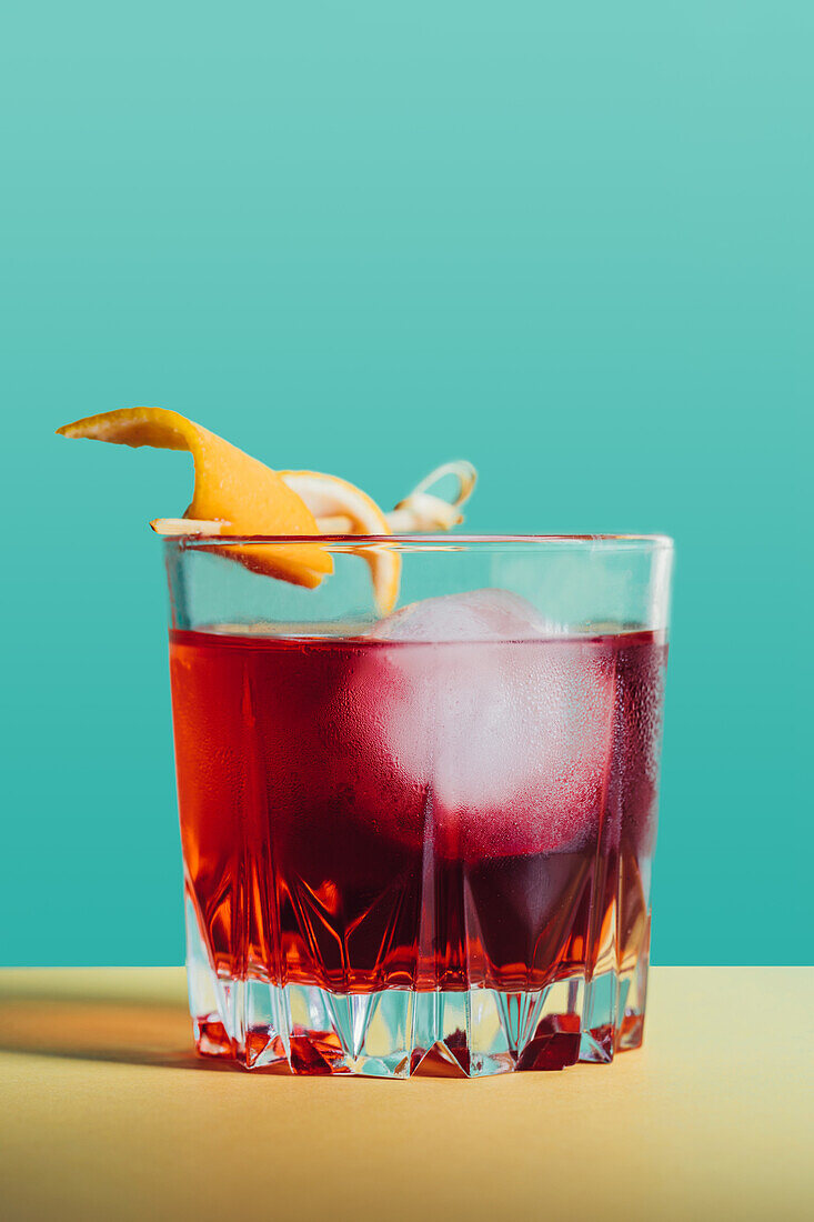 Glas mit bitterem alkoholischem Negroni-Cocktail, serviert mit Eis und Orangenschale auf einer hellen Fläche