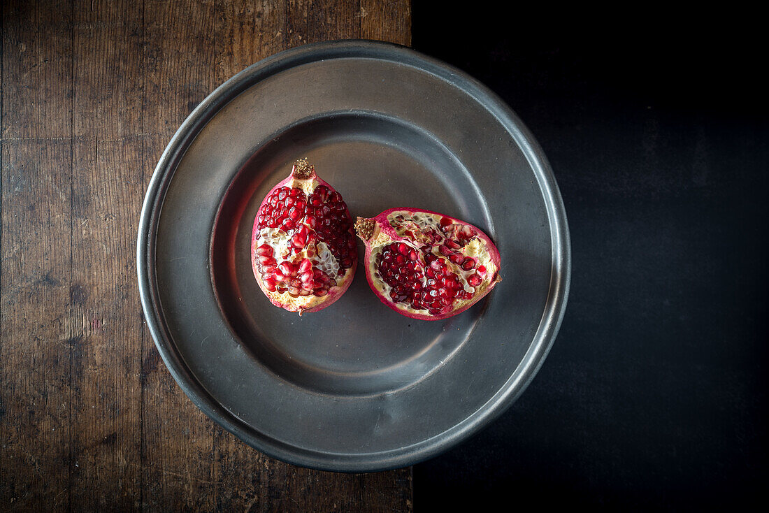 Overhead view of delicious ripe pomegranate pieces with bright juicy seeds on plate on brown background